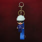 Keychain with character in blue outfit and white hair on a dark red background